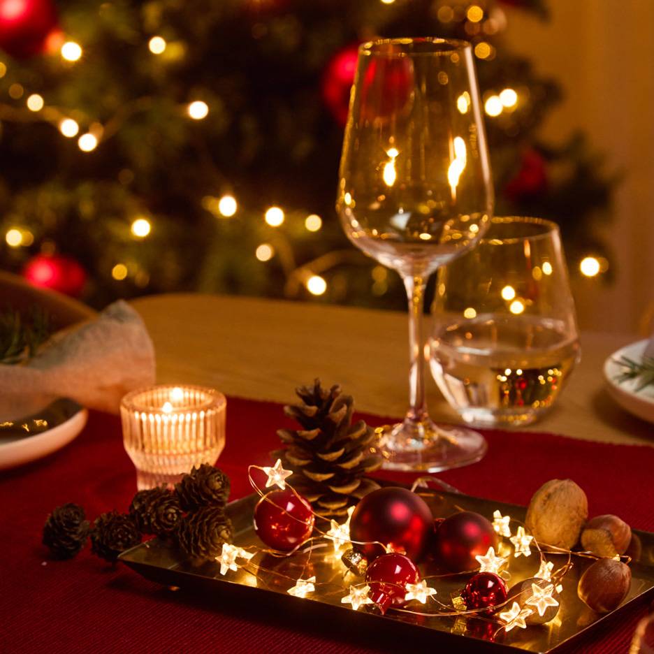 Kersttafeldecoratie met glazen, kaars en lichtsnoer.