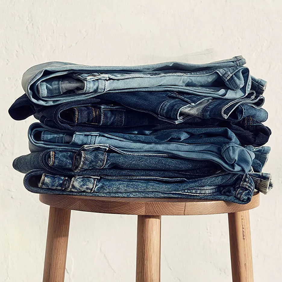 Een stapel jeans in verschillende blauwtinten op een houten krukje.