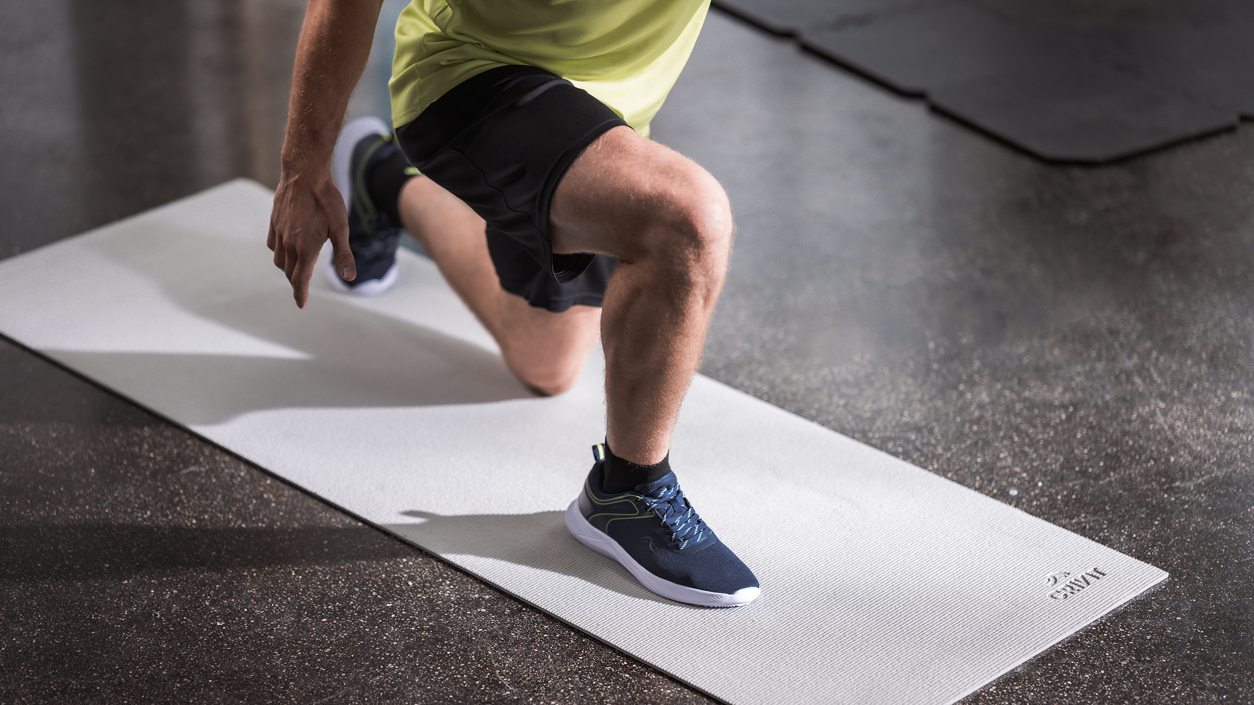 Homme en tenue de sport faisant des fentes sur un tapis d'exercice gris clair.