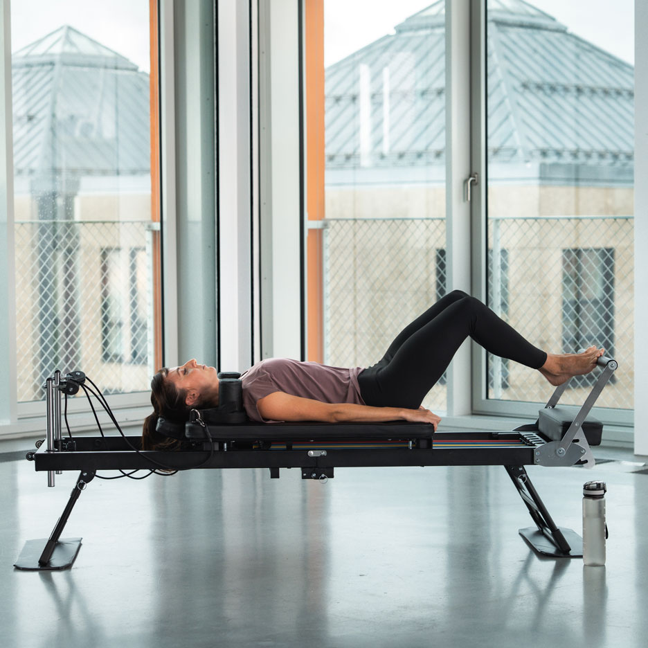 Vrouw doet Pilates op een reformer machine, met een waterfles ernaast.