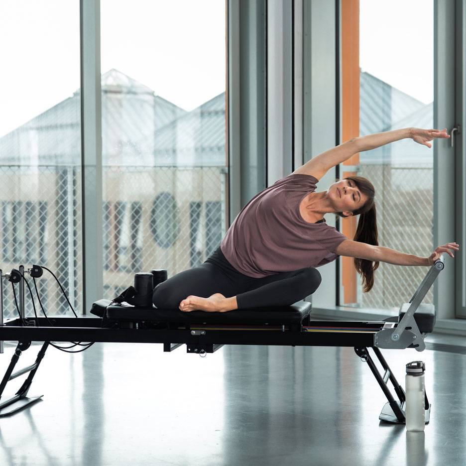 Vrouw doet pilates op een reformer, zijwaarts strekkend.