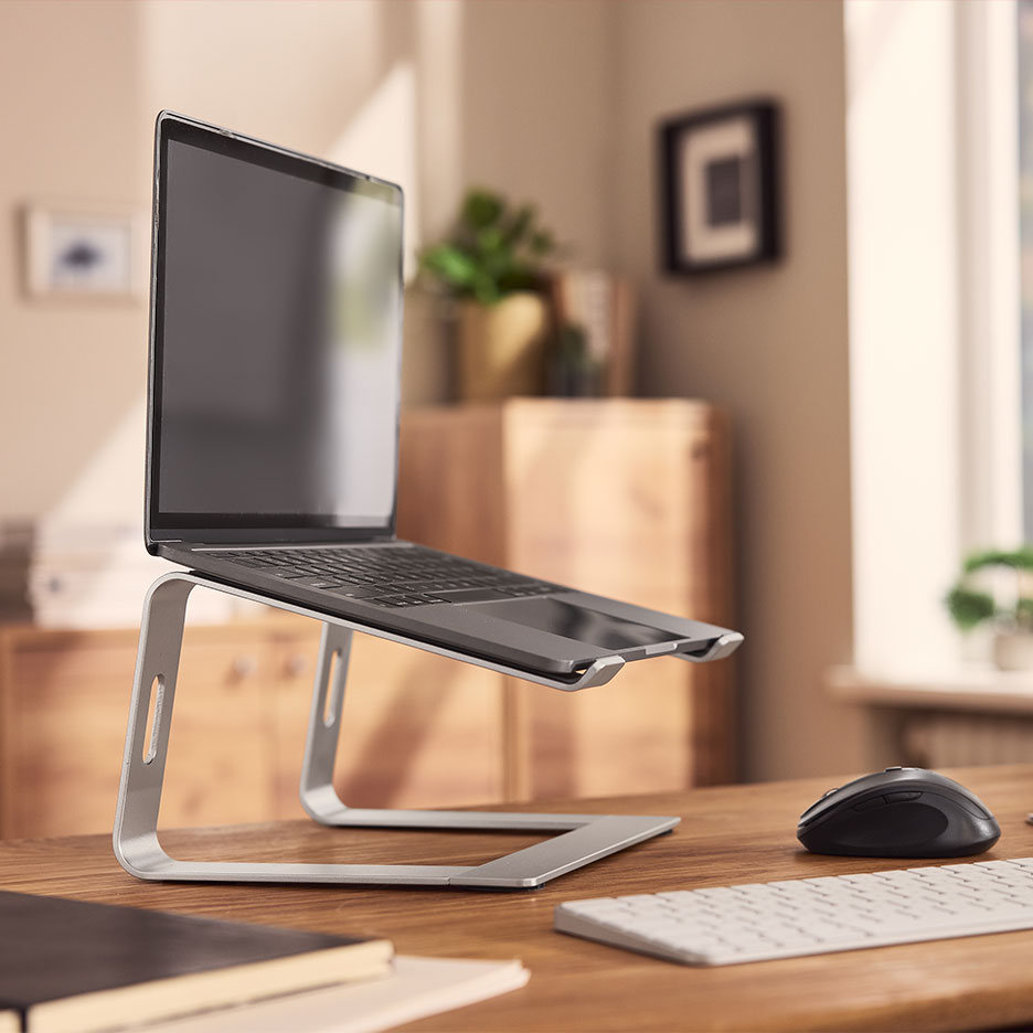 Zilveren laptopstandaard met een laptop op een houten bureau, met muis en toetsenbord.