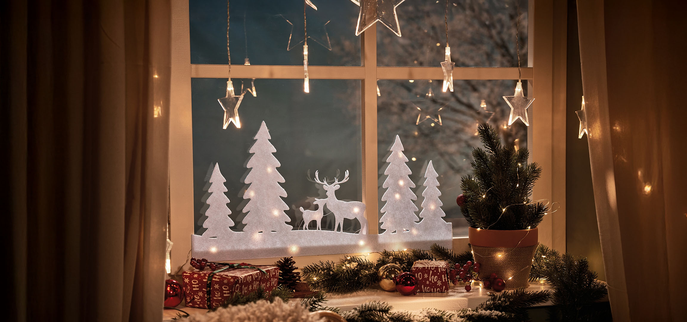 Kerstraamdecoratie met bomen, herten, cadeaus en lichtjes.