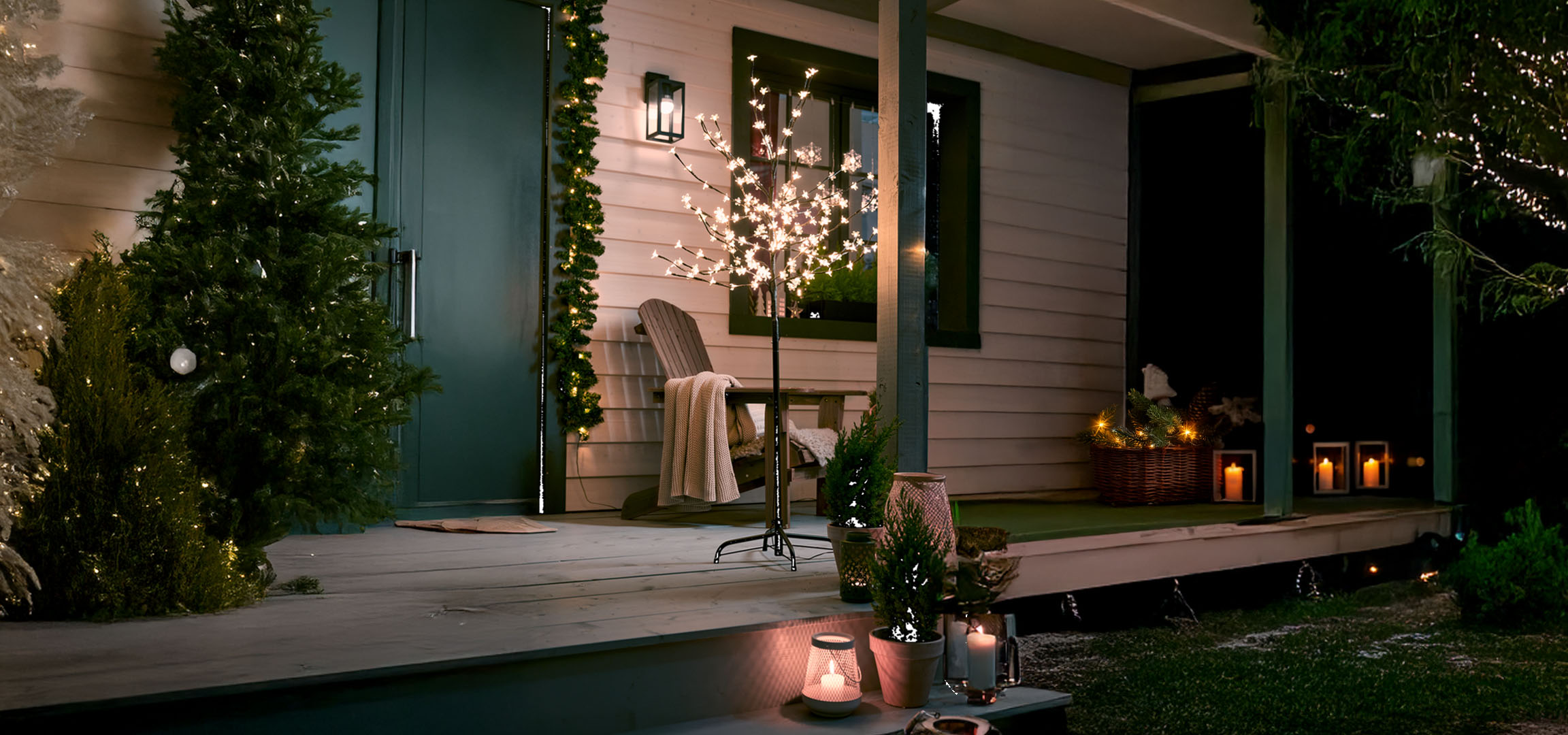 Huisveranda versierd met kerstverlichting, verlichte bomen en kaarsen.