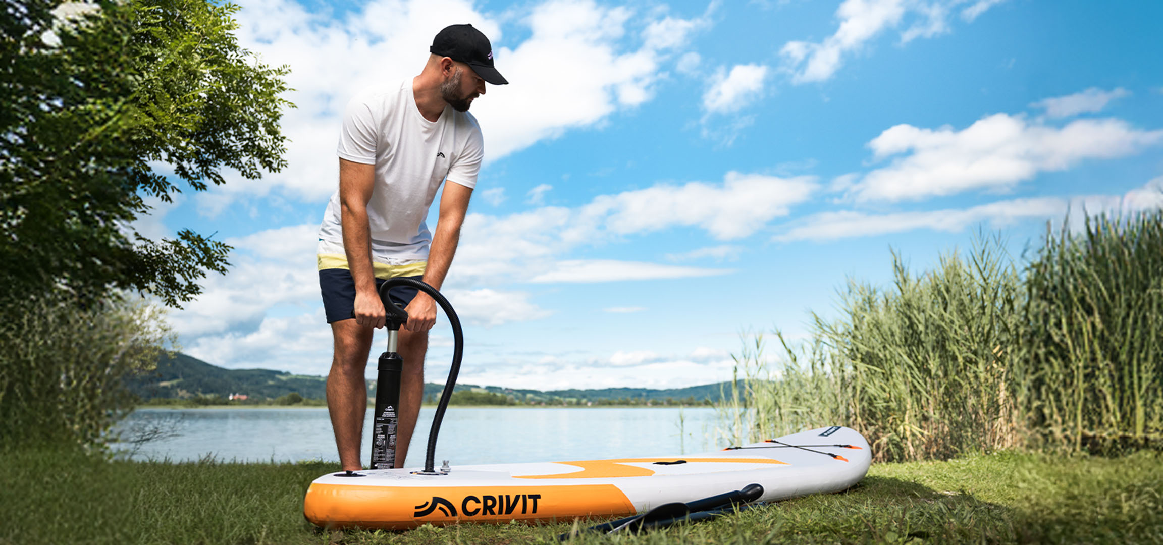 Man pompt CRIVIT SUP-board op bij een meer op groen gras.