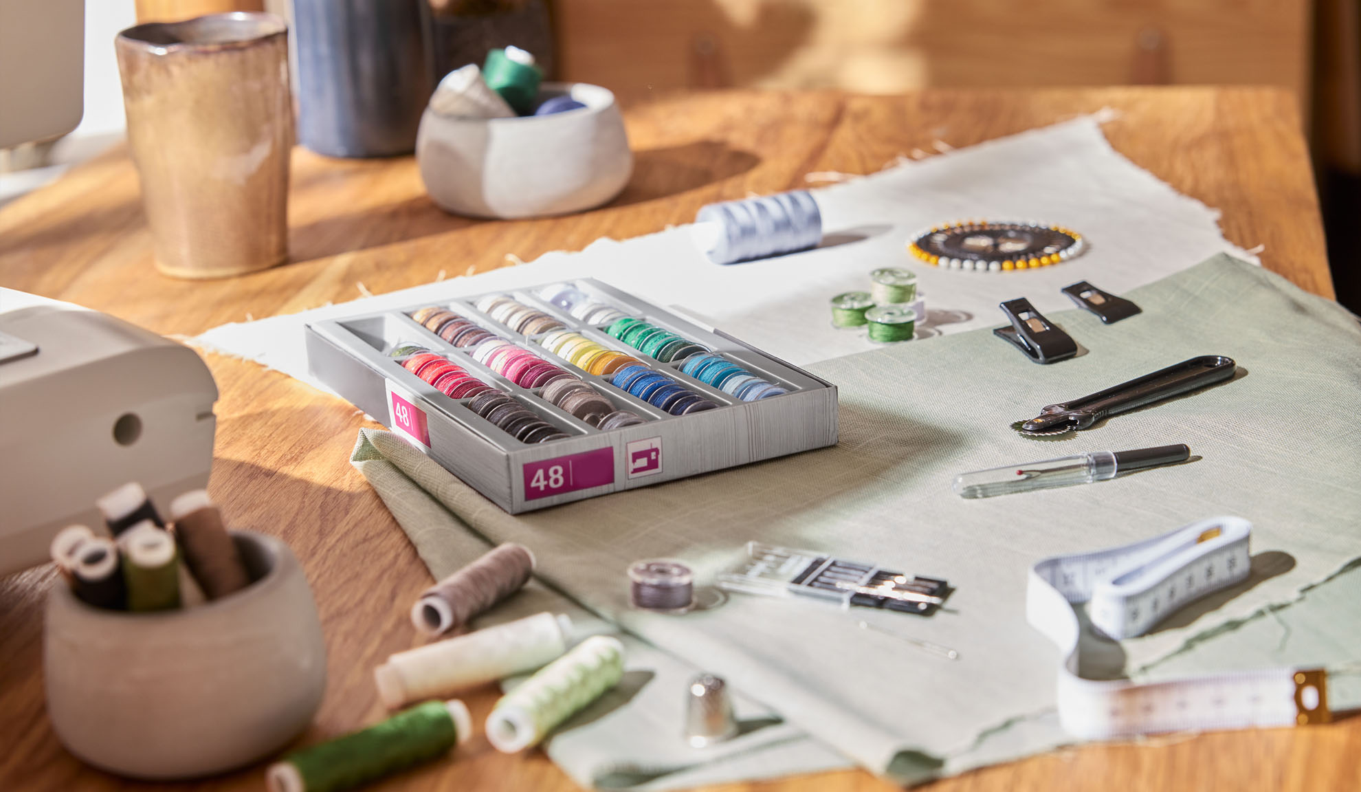 Kit de couture avec une boîte de fils colorés, une machine à coudre et divers outils sur une table en bois.