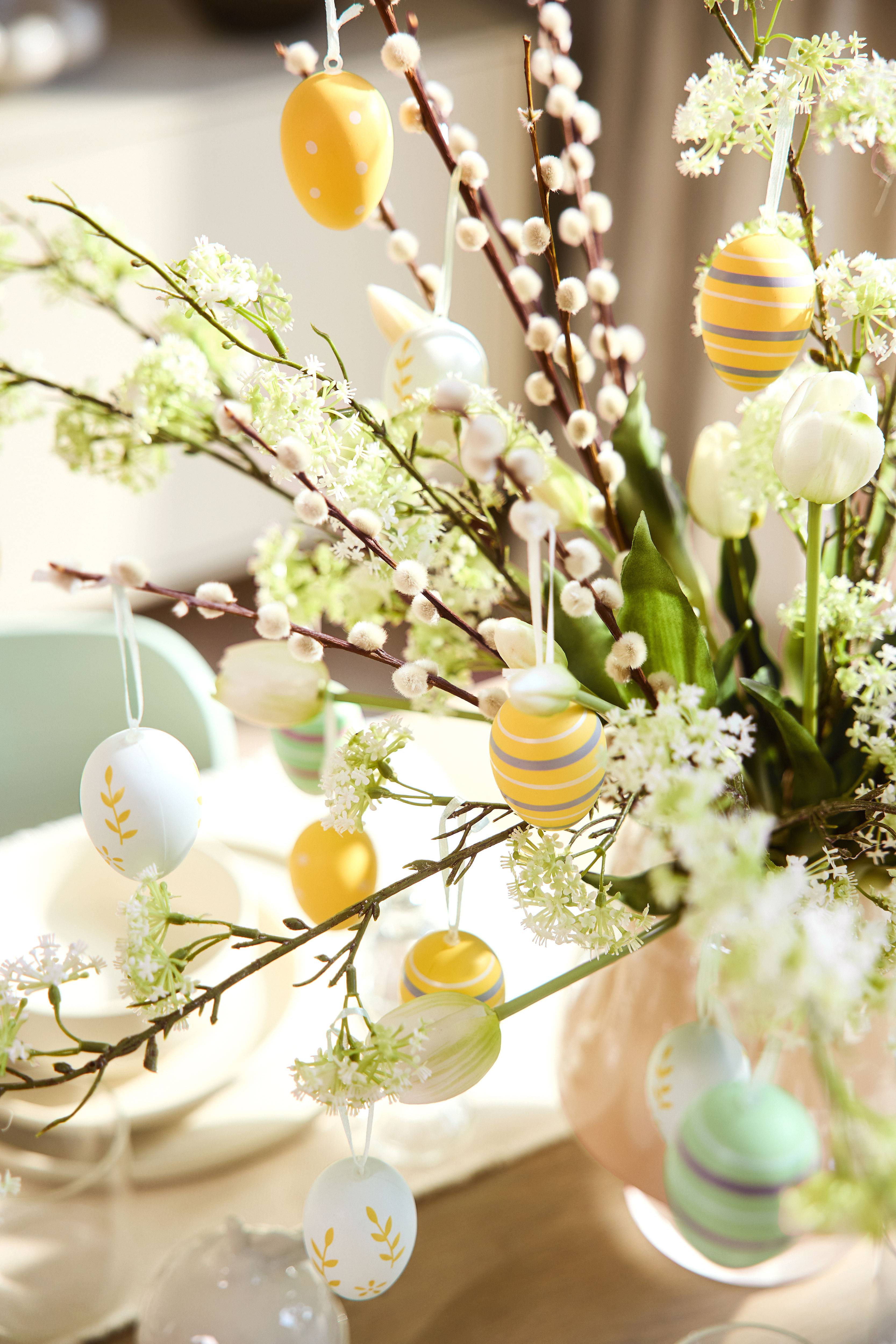 Paasdecoratie met wilgentakken, witte bloemen en kleurrijke eieren.