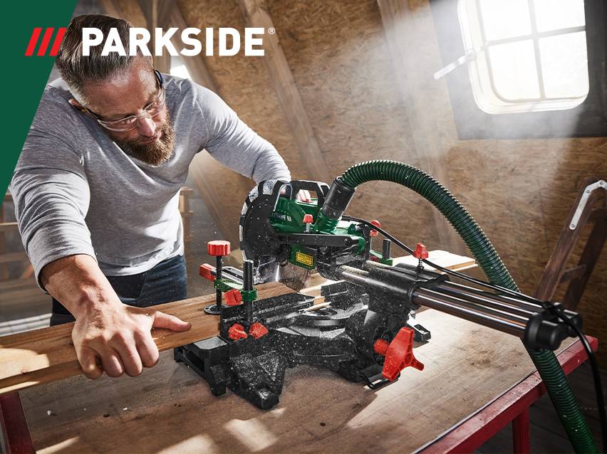 Man zaagt hout met een afkortzaag in een werkplaats.