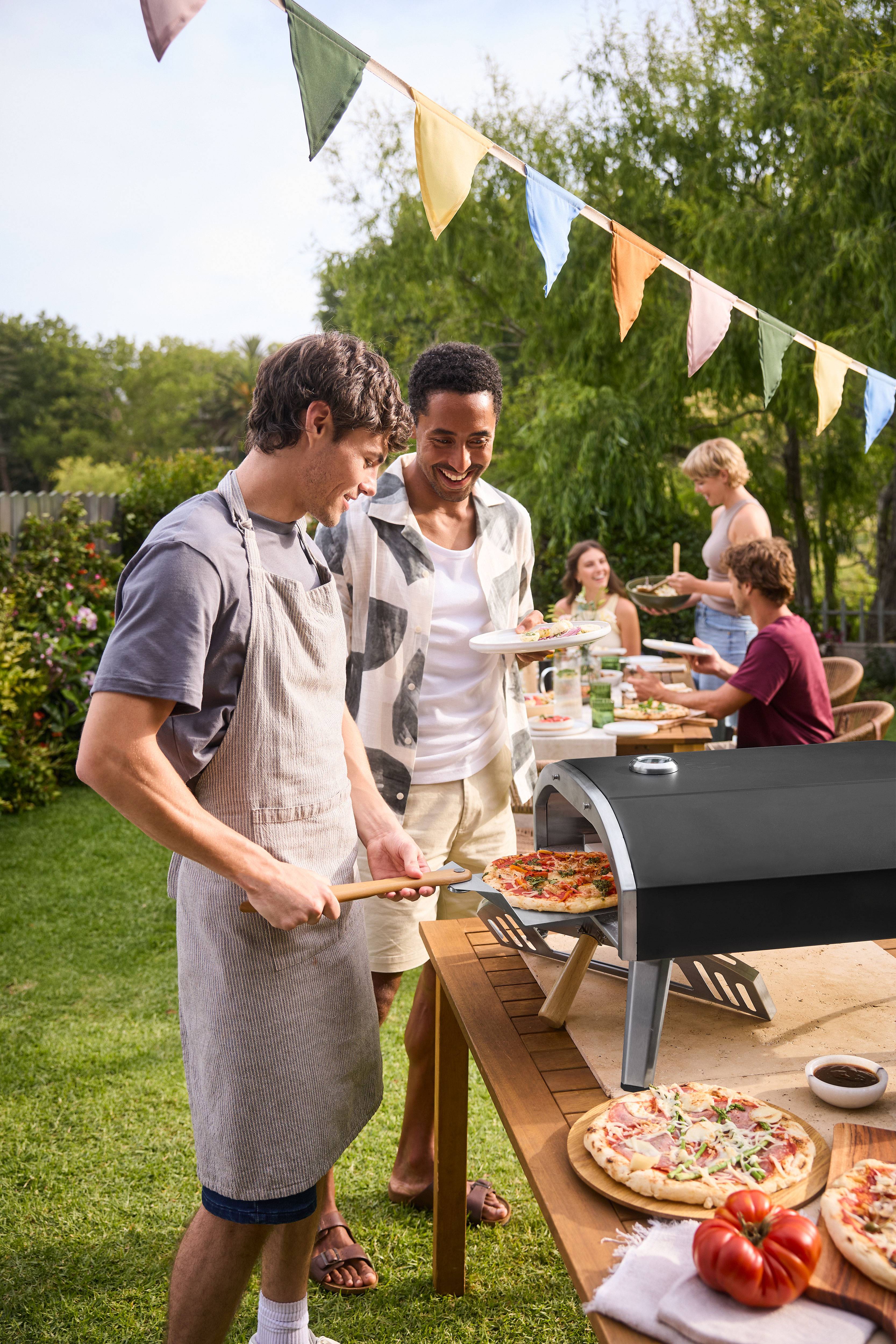 Mannen bakken pizza in een pizzaoven op een tuinfeest.