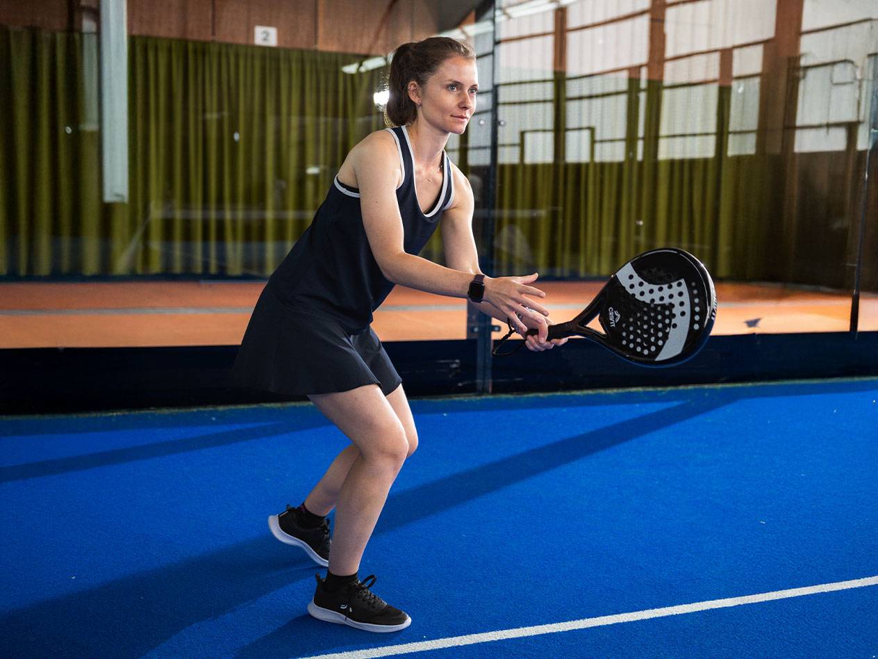 Lana Büttner in een zwarte padeljurk met een zwart padelracket op een blauw terrein.