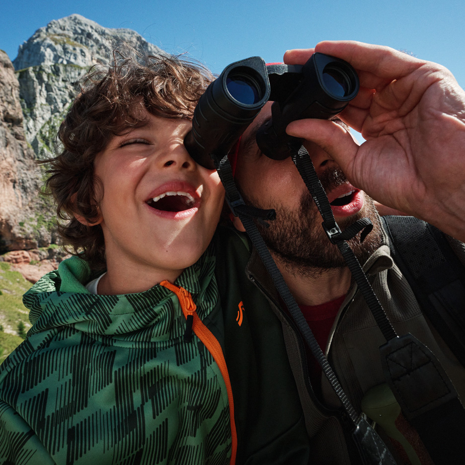 Vader en zoon verkennen bergen met verrekijker, dragen outdoor jassen.
