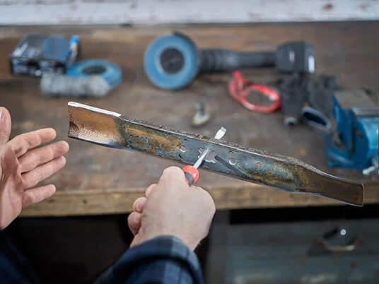 Mains affûtant une lame de tondeuse sur un établi avec des outils.