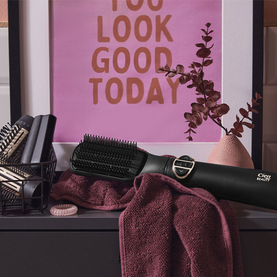 Cien Beauty stijltangborstel op een handdoek, met haaraccessoires en een poster.