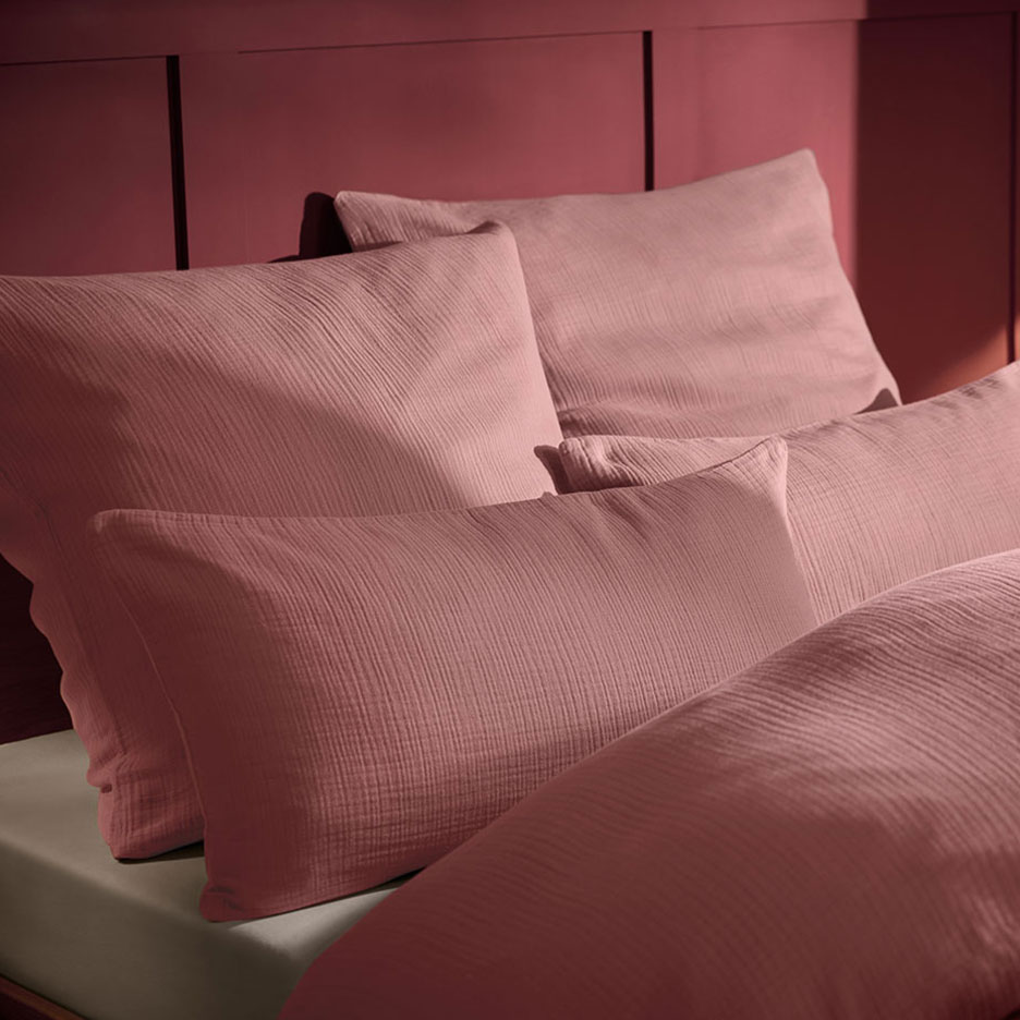 Roze mousseline kussen en beddengoed op een bed met een houten hoofdbord.