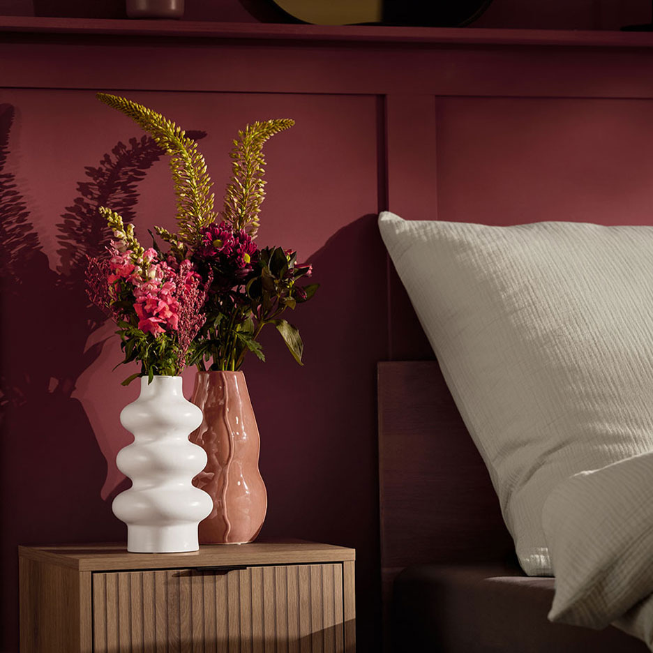 Twee vazen met bloemen op een nachtkastje naast een bed met een wit kussen.