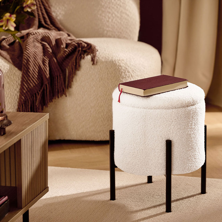 Witte pluizige kruk met zwarte poten, een rood boek, fauteuil en bruine deken.