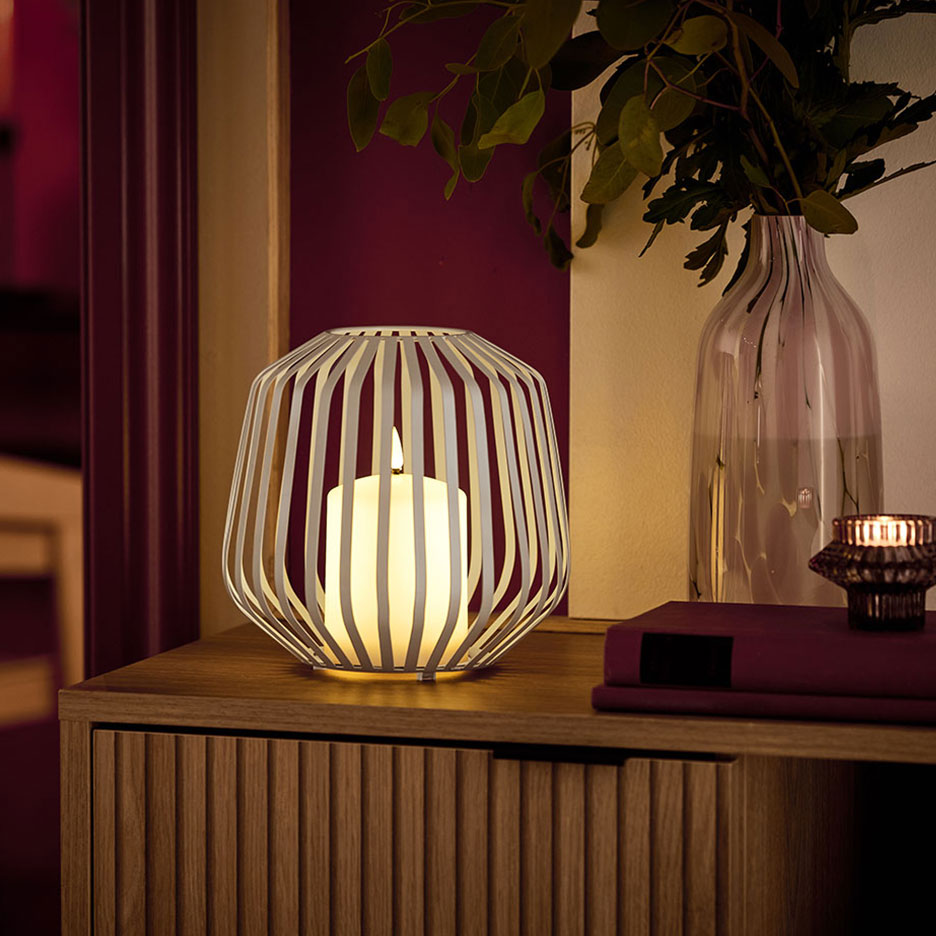 Een LED-kaars in een witte metalen houder op een houten ladekast.