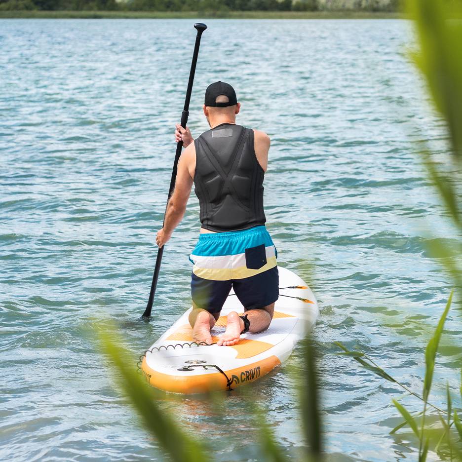 Man peddelt op een meer op een Crivit SUP-board, met zwemvest en zwembroek.