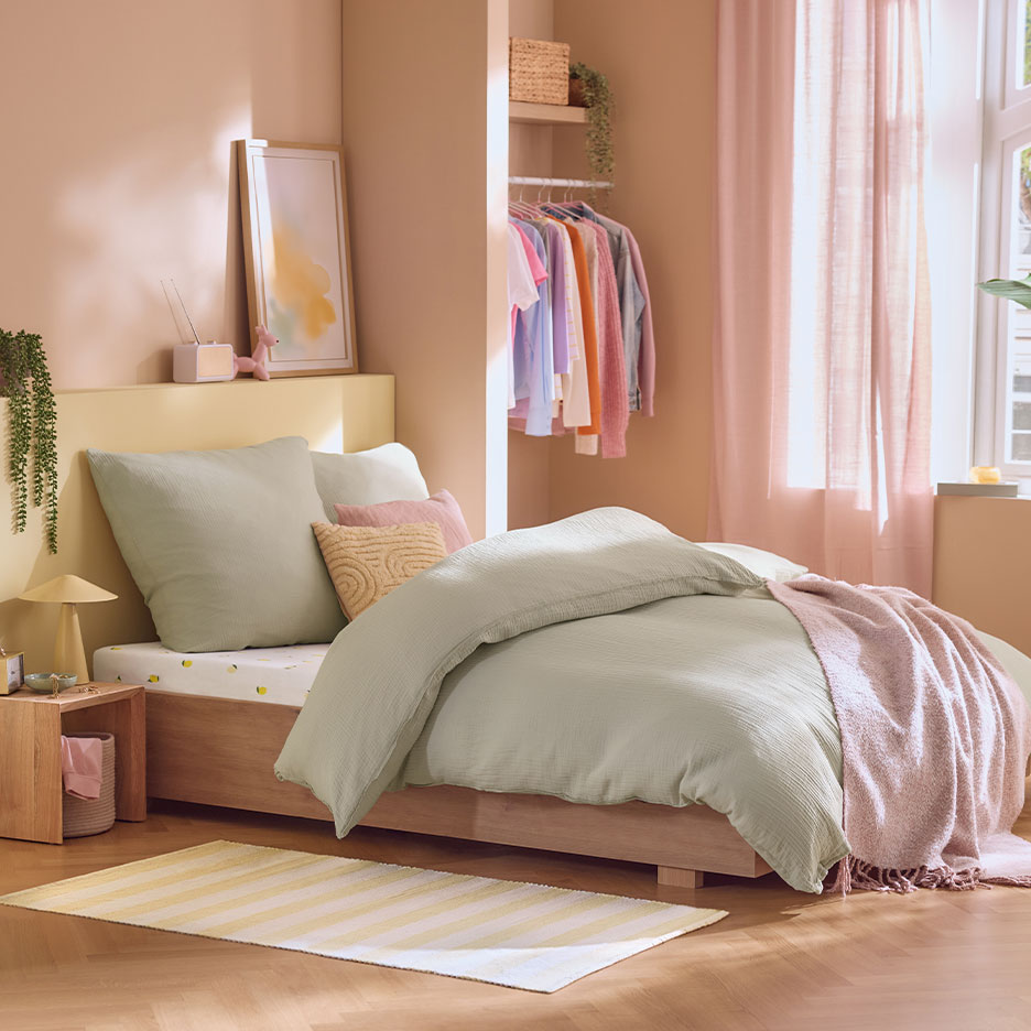 Slaapkamer met houten bed, lichtgroen beddengoed, roze gordijnen en open kledingkast.