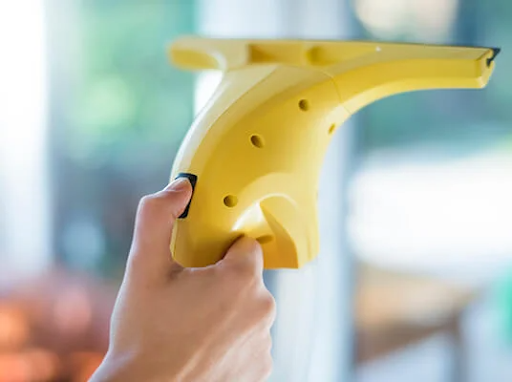 Hand houdt een gele elektrische raamreiniger vast, een raam schoonmakend.