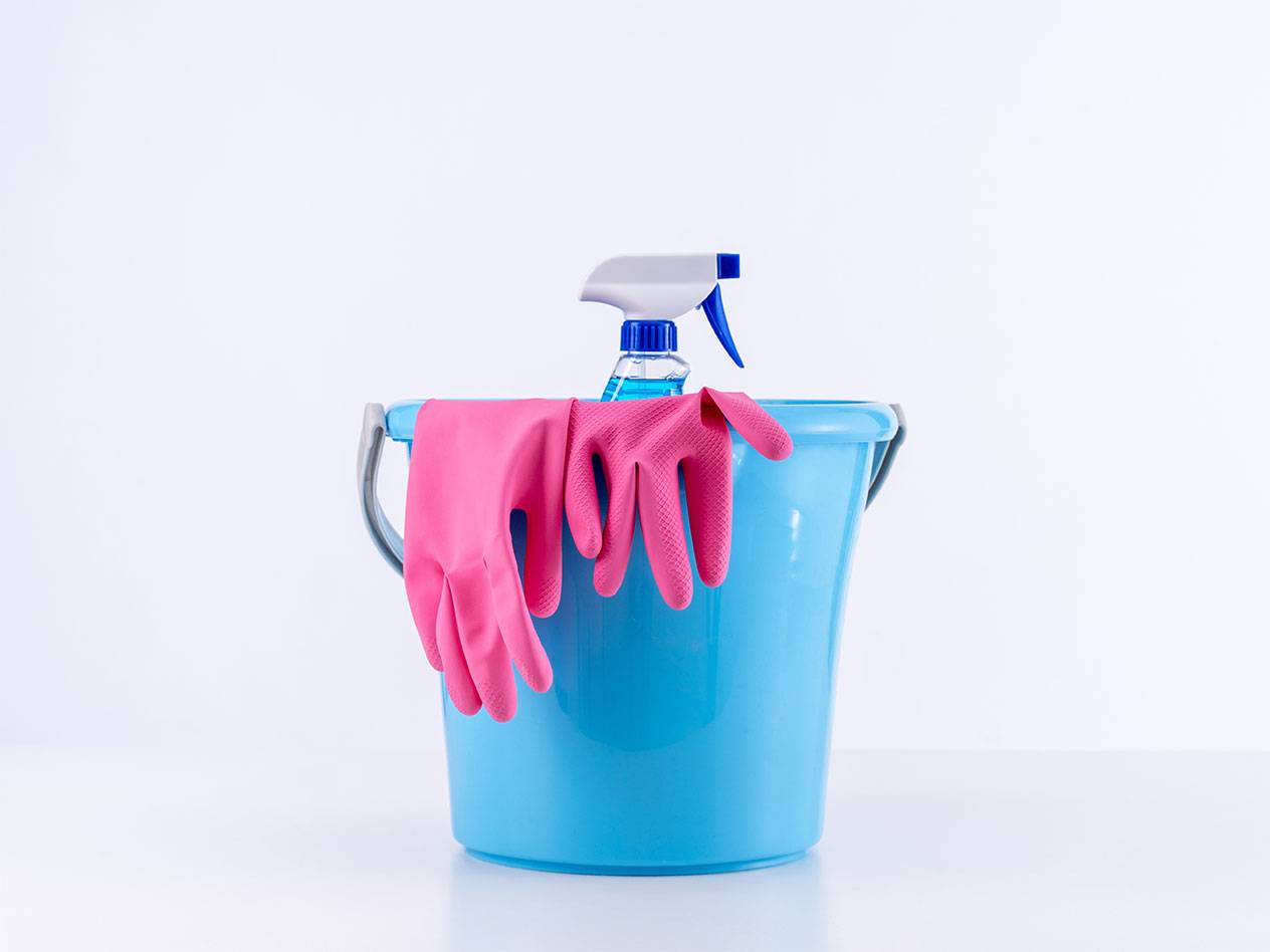 Blauwe emmer met roze schoonmaakhandschoenen en een spuitfles.
