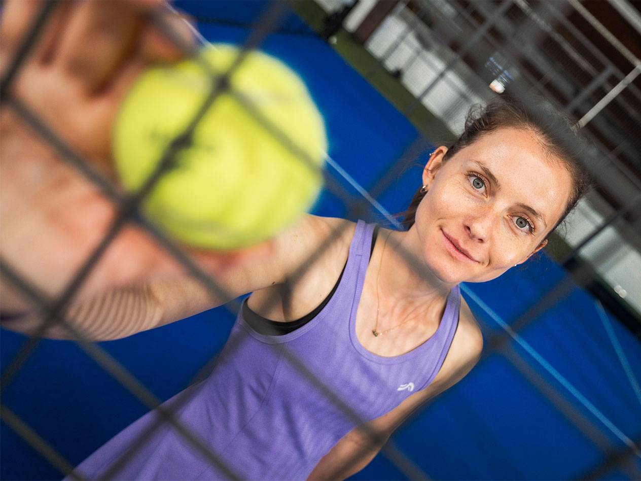 Lana Büttner in sportkleding houdt een padelbal door een net, met een blauw terrein op de achtergrond.