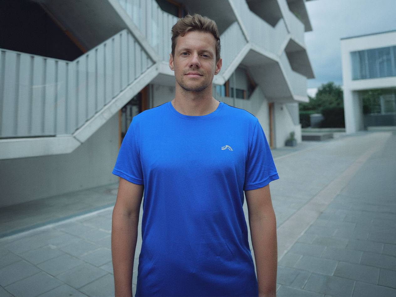 Man in blauw Crivit sportshirt, met modern gebouw op de achtergrond.