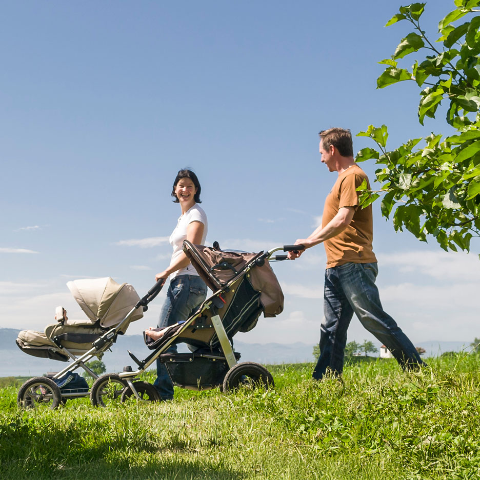 Een gezin wandelt in een weide met een kinderwagen.
