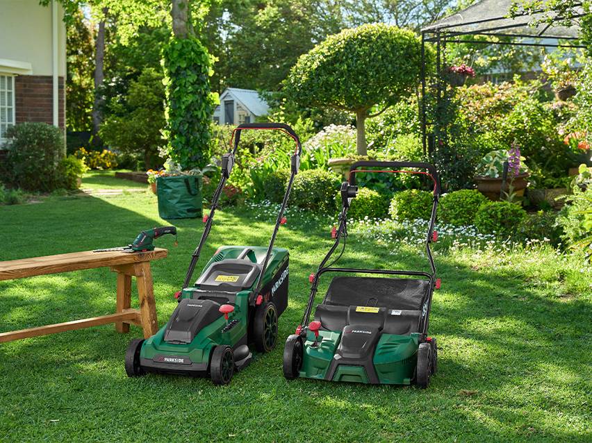 Twee grasmaaiers en een heggenschaar op een houten bank in een groene tuin.