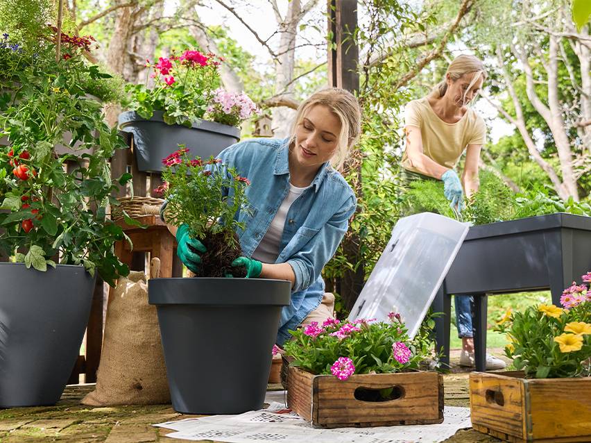 Vrouwen planten bloemen en groenten in potten en verhoogde plantenbakken in een tuin.