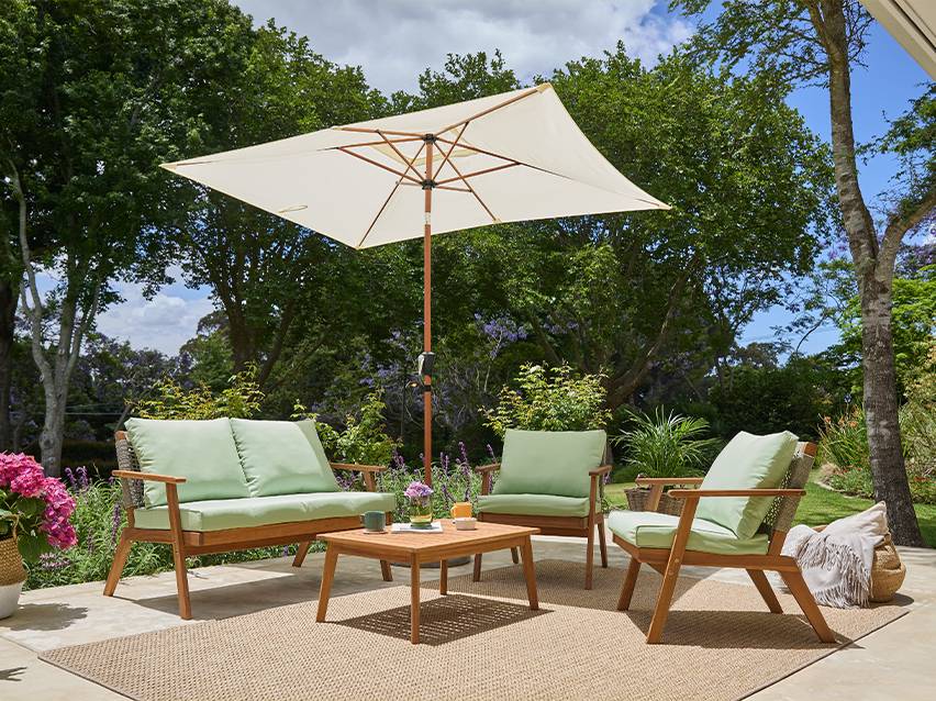 Houten loungeset met lichtgroene kussens en parasol op een terras.