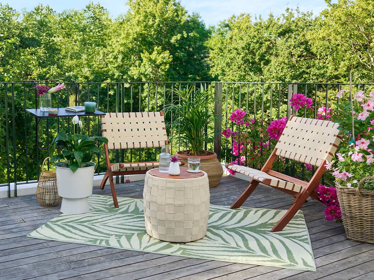 Balkon met houten vloer, stoelen met gevlochten rugleuningen, een tafel en planten.