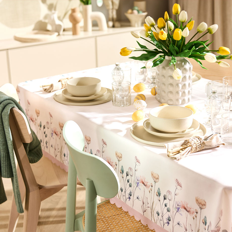 Paastafel met bloemen tafelkleed, gele tulpen en servies in natuurlijke kleuren.