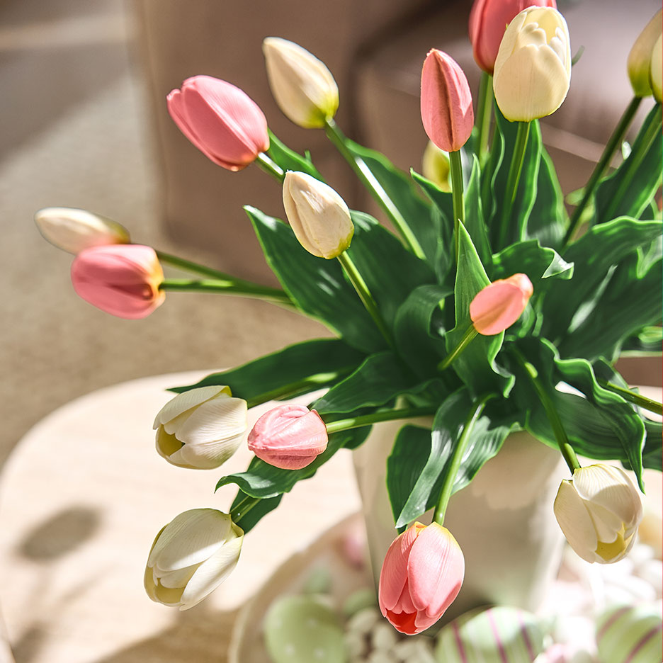 Roze en witte tulpen in een vaas, met paaseieren op een dienblad op de achtergrond.