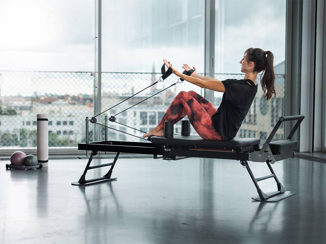 Vrouw doet Pilates op een reformer met uitzicht op de stad.