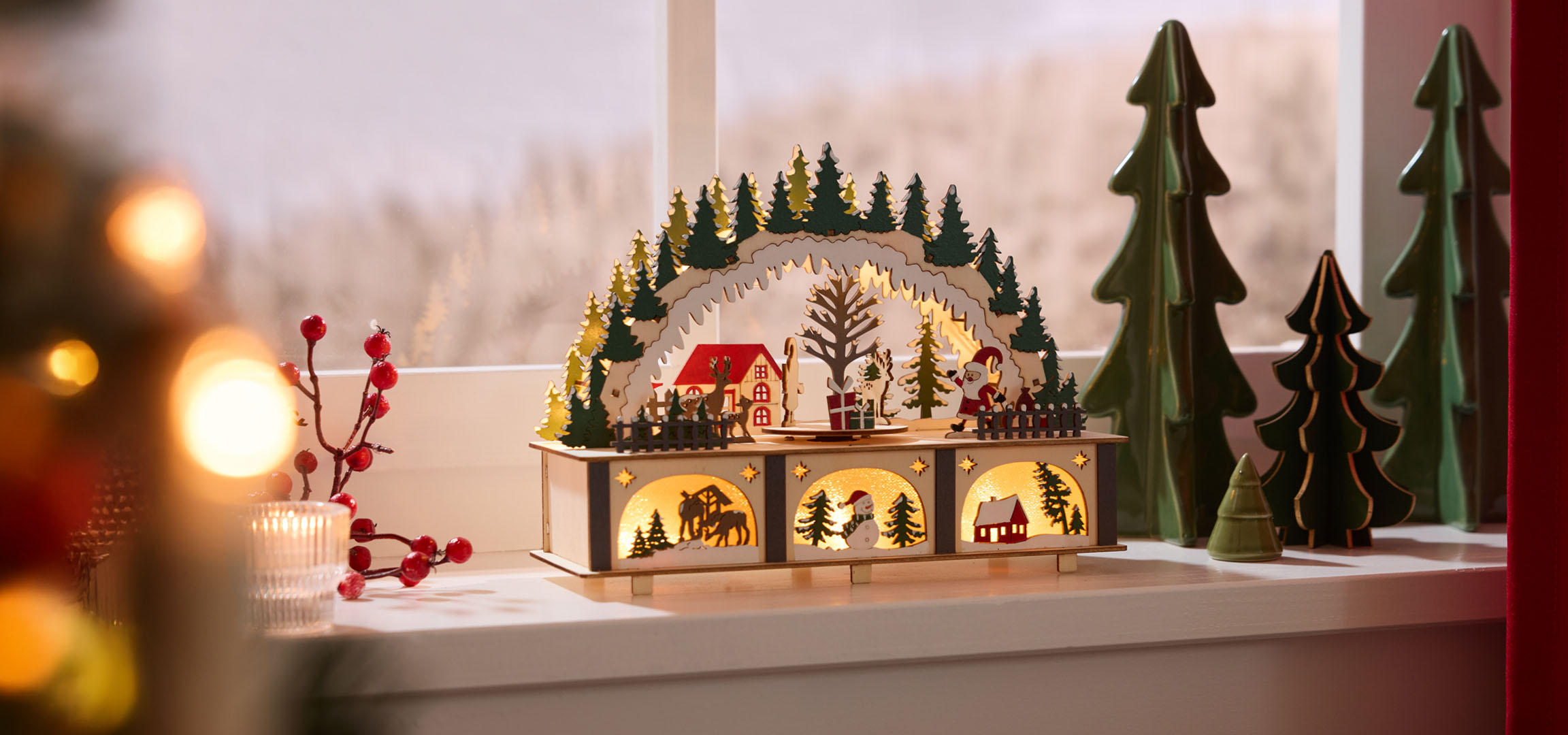 Kerstdecoraties: verlicht houten landschap met huizen en bomen, rode bessen en kaars.