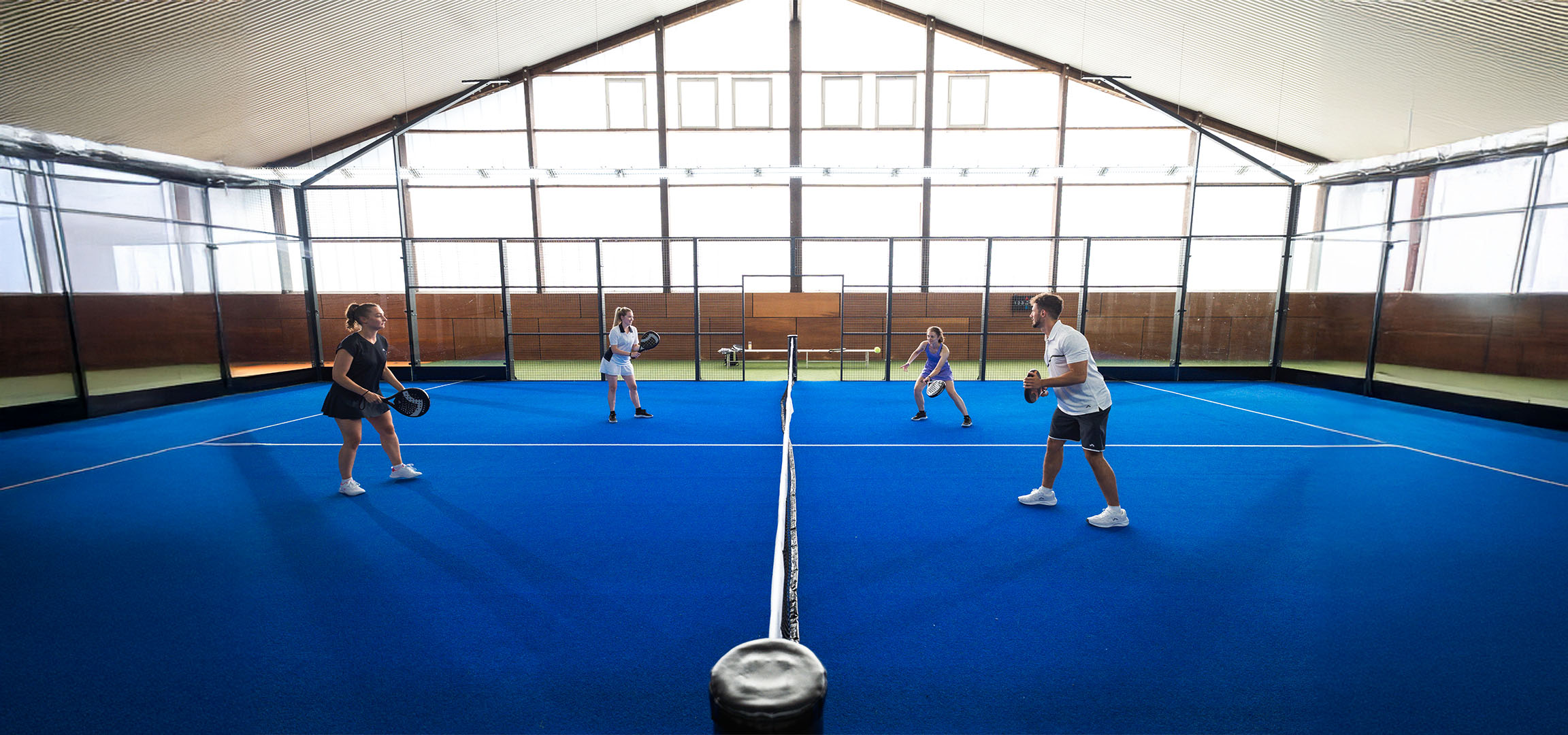 Vier mensen spelen padel op een blauw veld, met rackets en sportkleding.