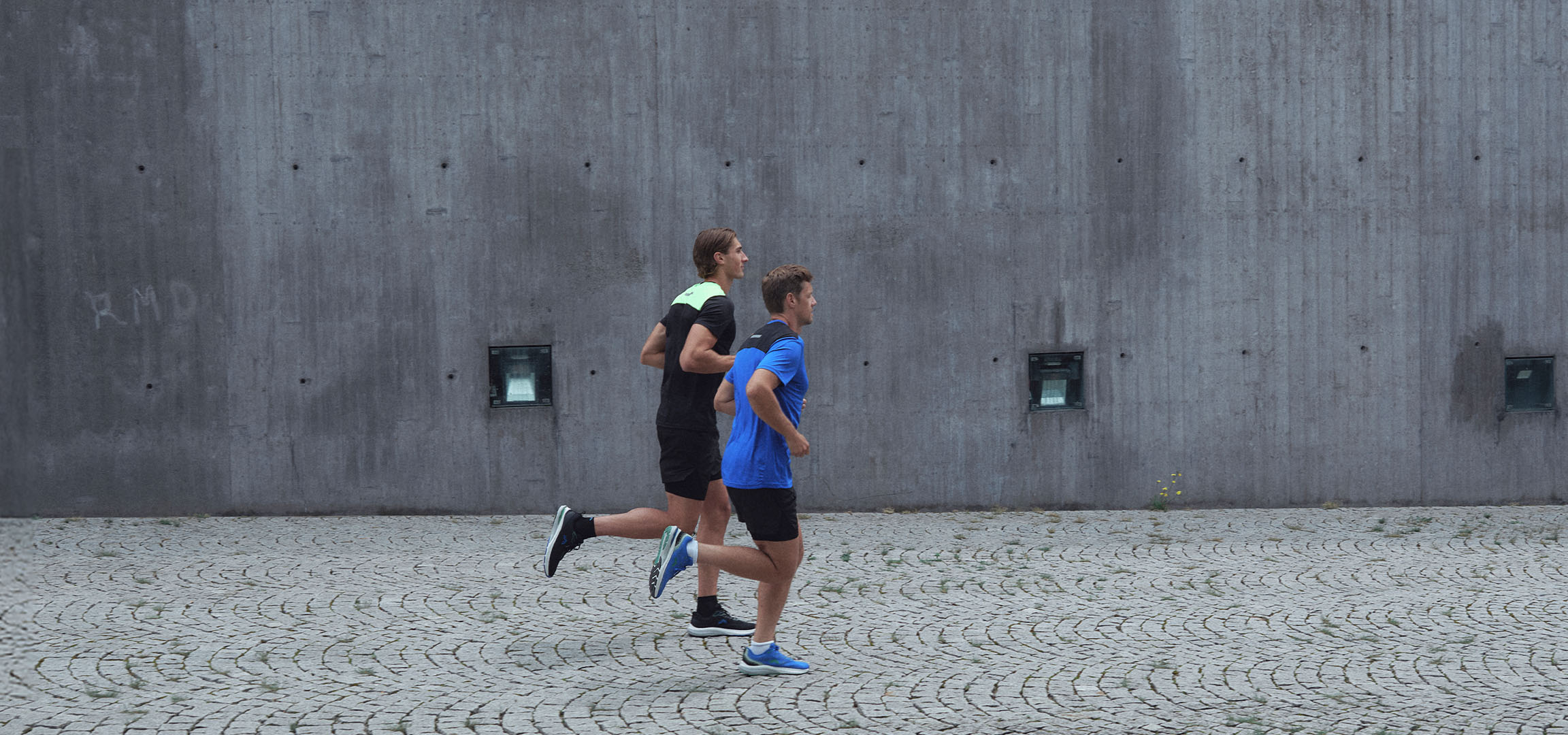 Deux hommes en tenue de sport courent le long d'un mur.