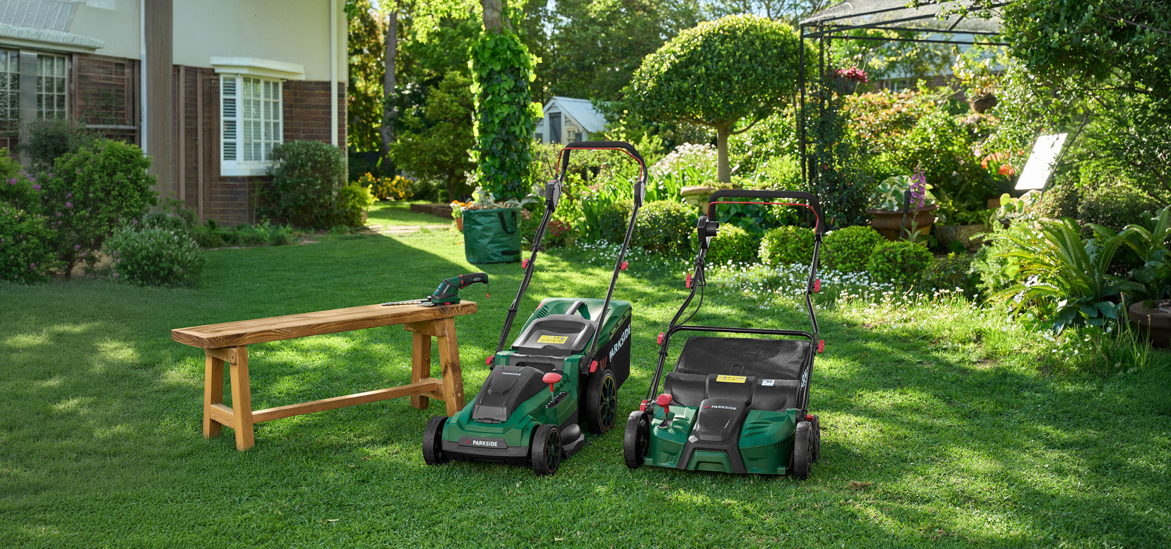 Deux tondeuses à gazon et un taille-haie dans un jardin verdoyant.