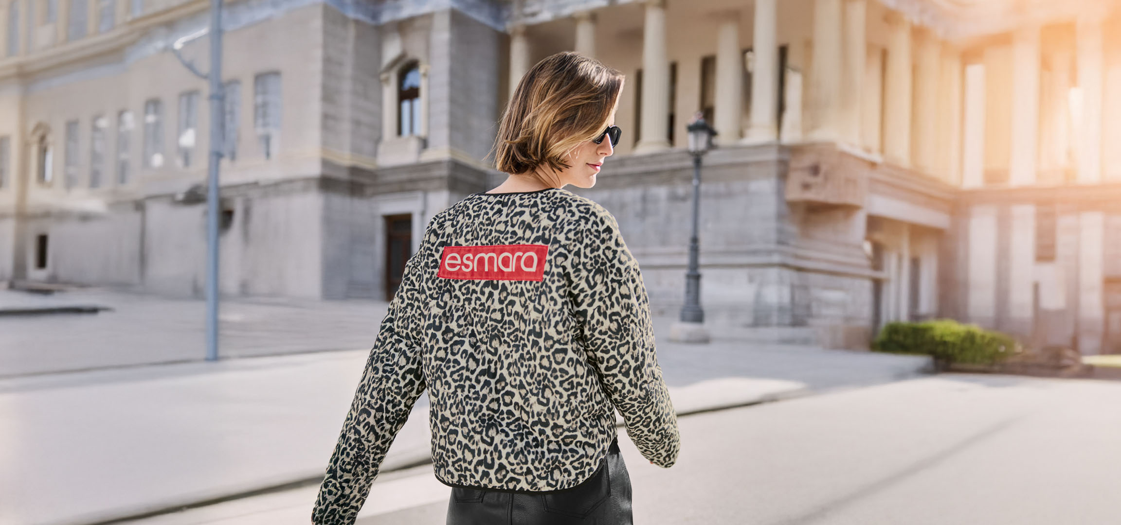 Vrouw in Esmara luipaardjas, zonnebril, op een stedelijke straat.