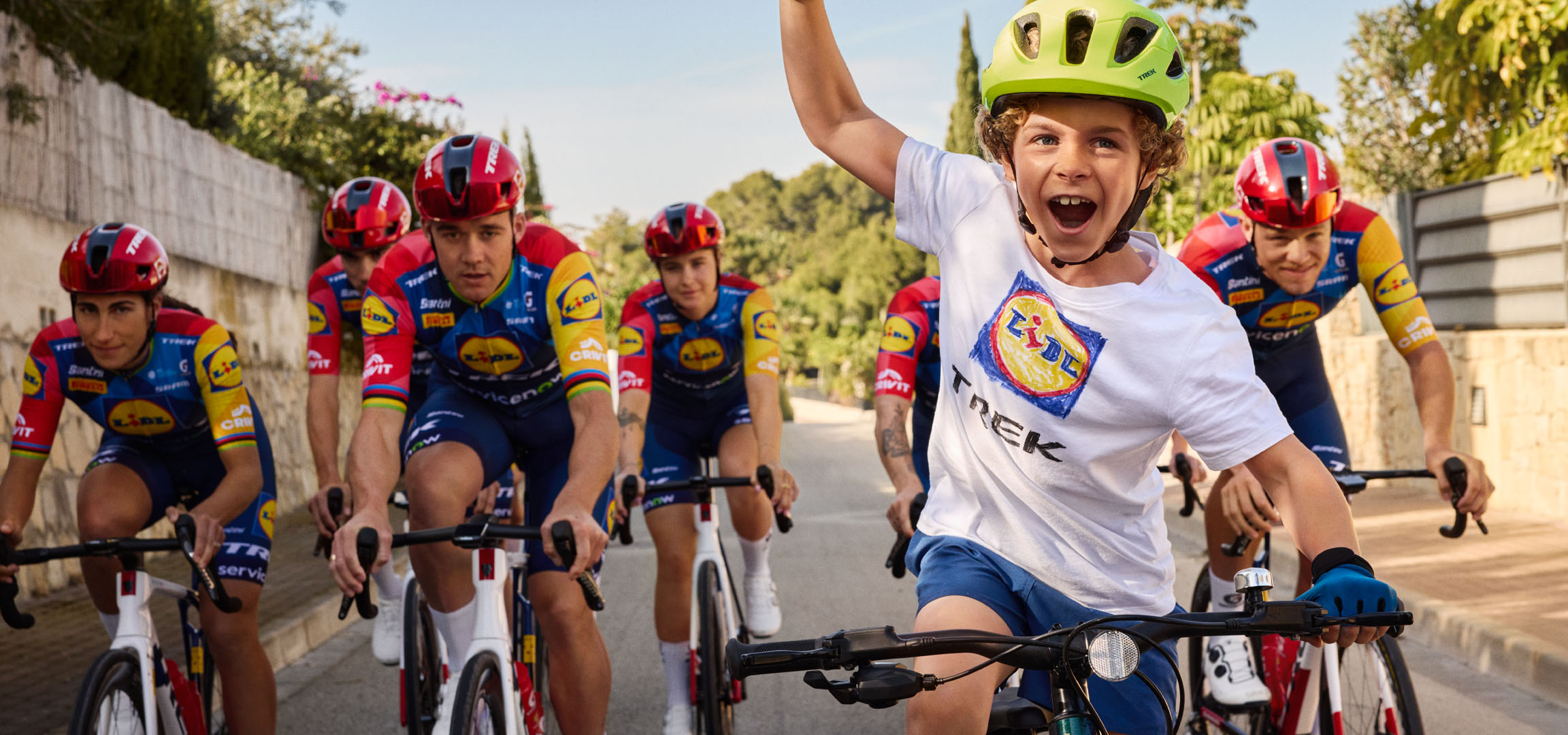 Kind met helm en T-shirt met Lidl-logo, omringd door fietsers.