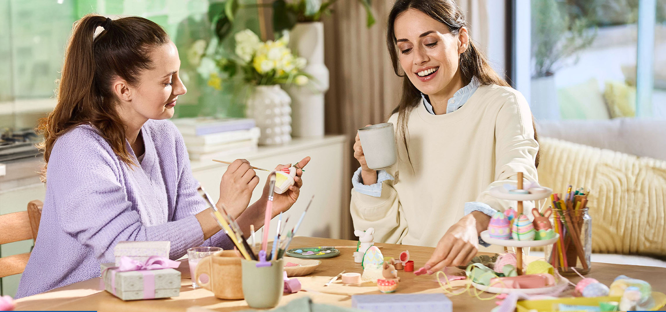 Twee vrouwen versieren paaseieren en figuren aan een tafel.