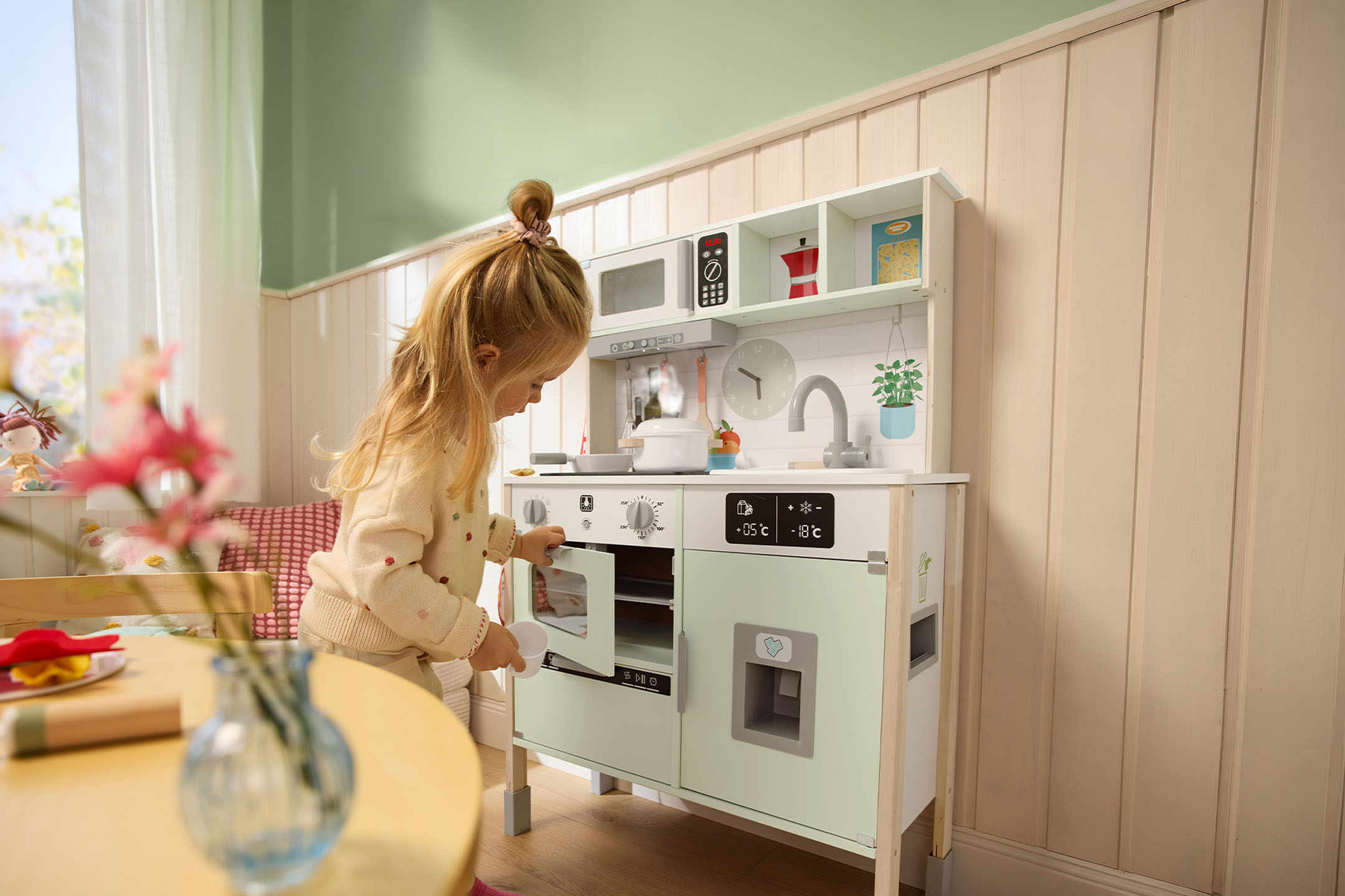 Klein meisje speelt met een houten speelkeuken, de ovendeur openend.