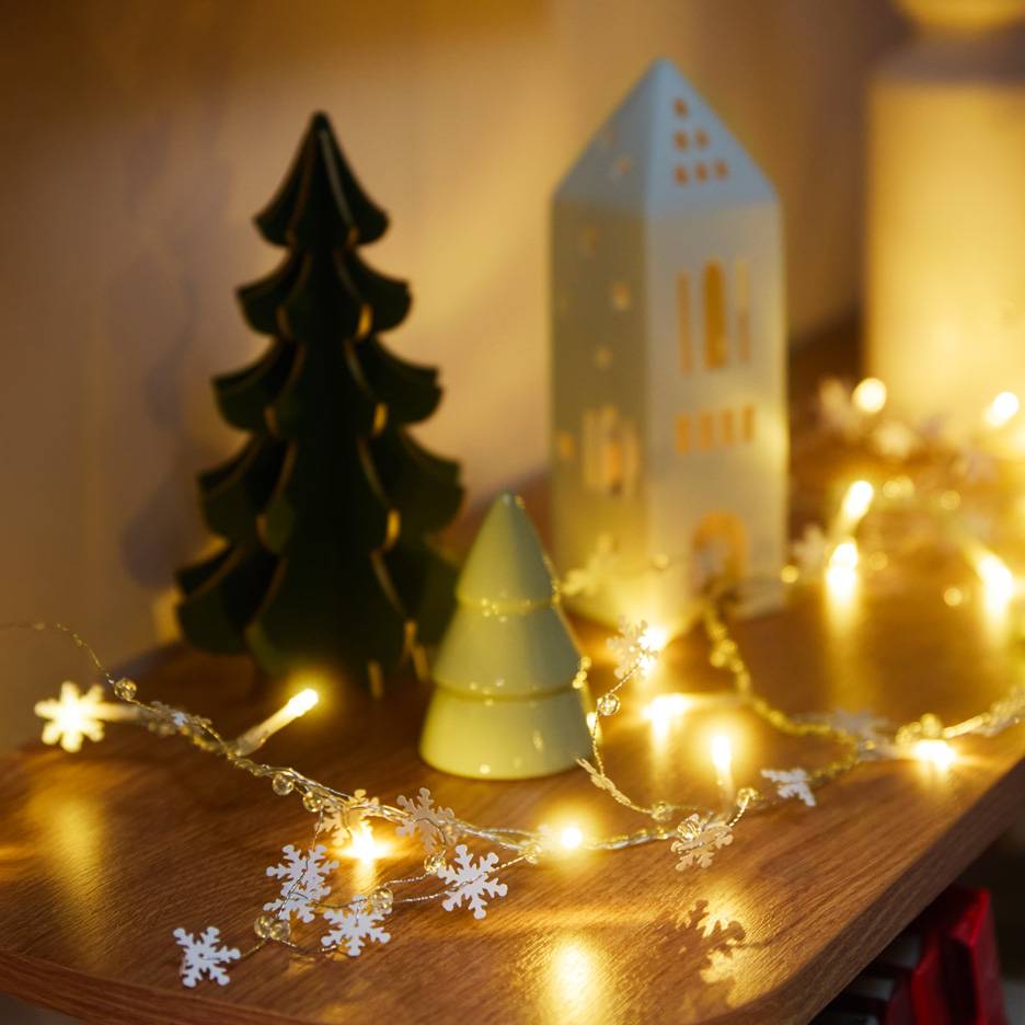 Kerstdecoraties: een donkergroene boom, een lichtgroene boom, een wit huis en een sneeuwvlokken lichtslinger.