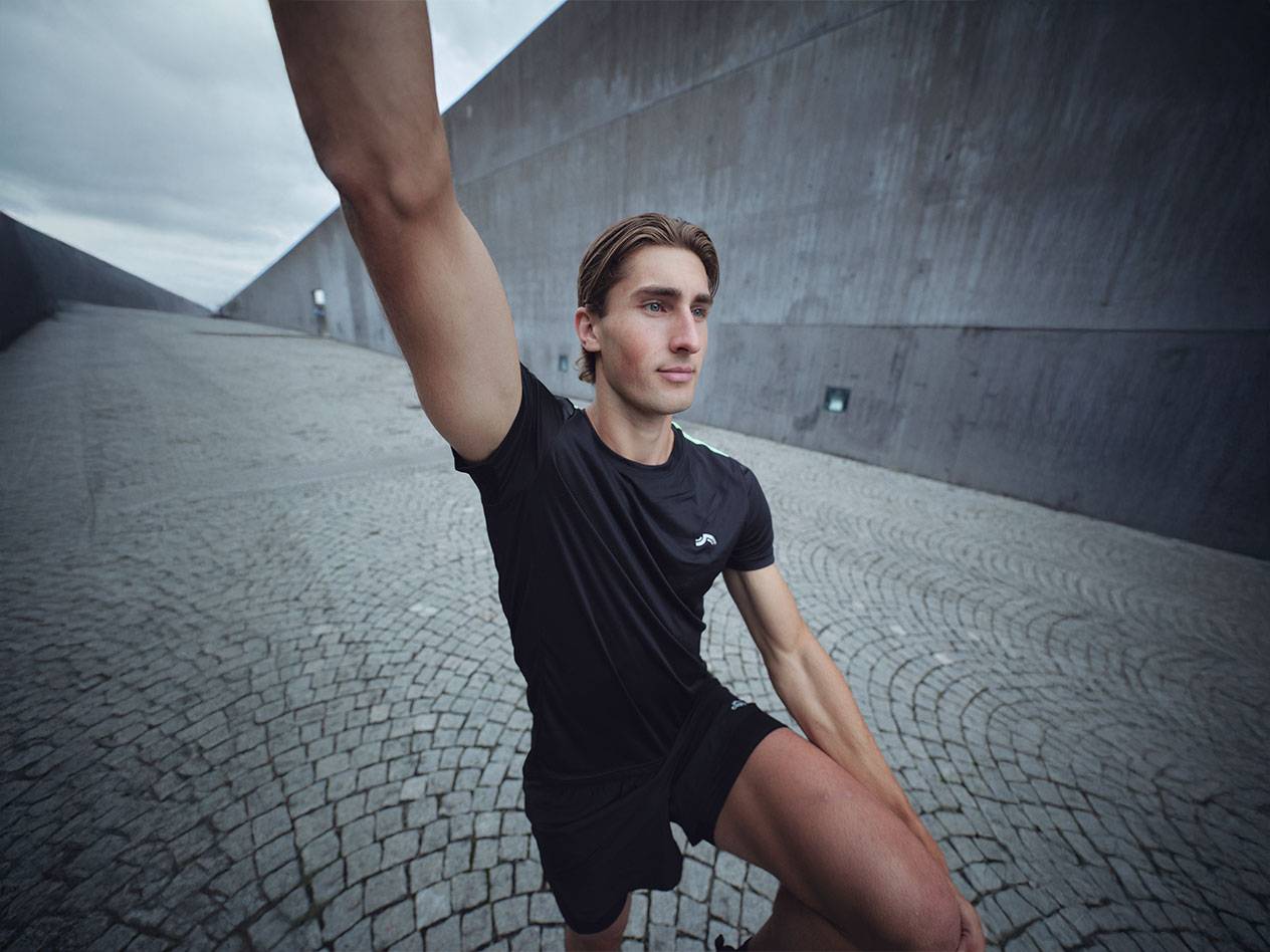 Homme en t-shirt et short de sport Crivit noirs s'étirant à l'extérieur.