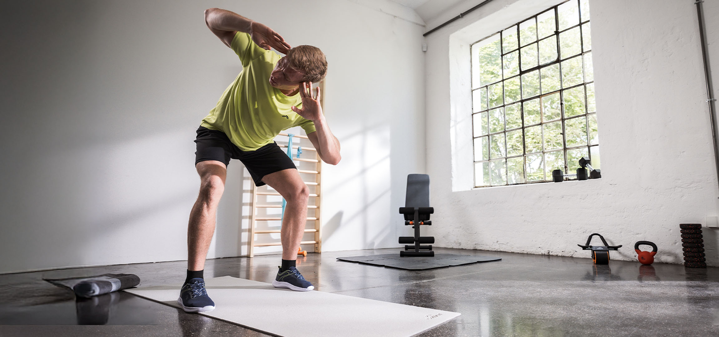 Homme s'entraînant dans une salle de sport, utilisant un tapis de yoga et des haltères.
