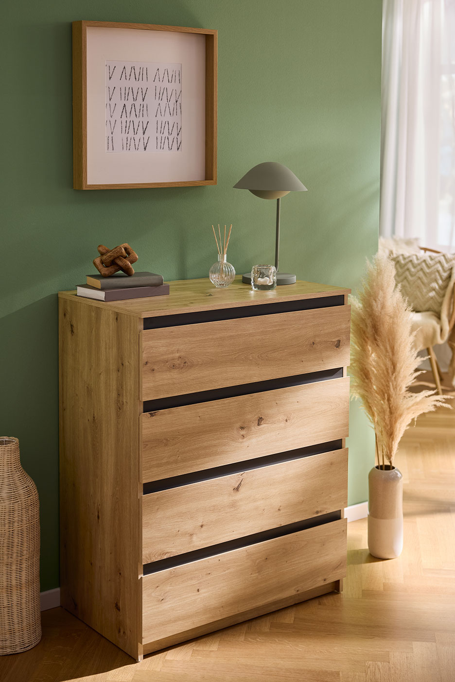 Houten ladekast met vier laden met zwarte handgrepen, versierd met een ingelijste afbeelding en lamp.