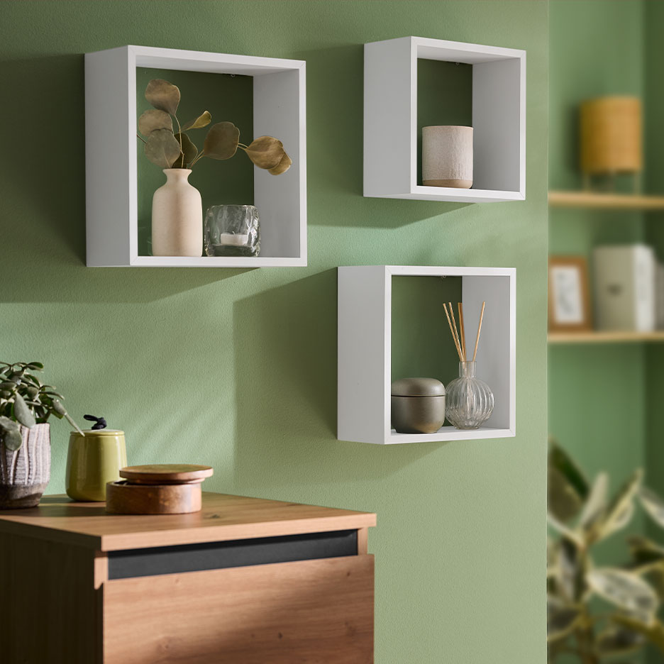 Witte wandplanken met decoratie op een groene muur, met een houten ladekast eronder.