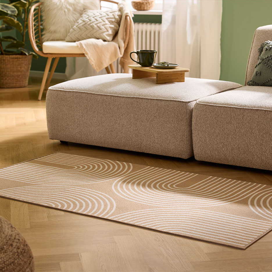 Beige vloerkleed met boogpatroon, modulaire bank en houten fauteuil in een gezellige woonkamer.