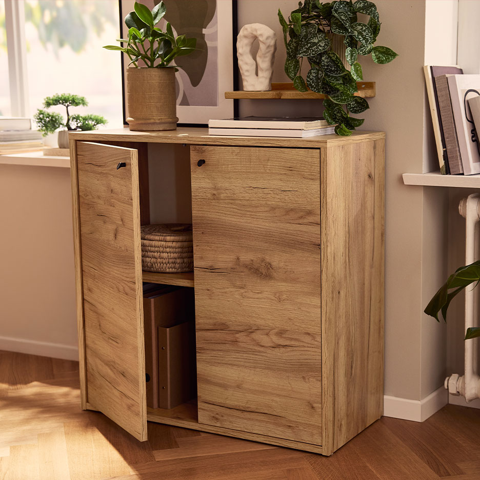 Lichte houten kast met twee deuren, één open, in een lichte kamer met planten en boeken.